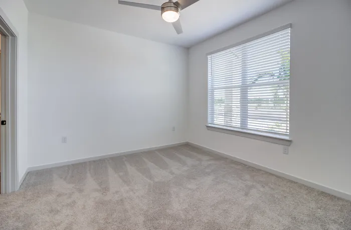 Unfurnished primary bedroom with carpet, large window, ceiling fan, and overhead lighting at Garrett Forum in Fort Myers, Florida.