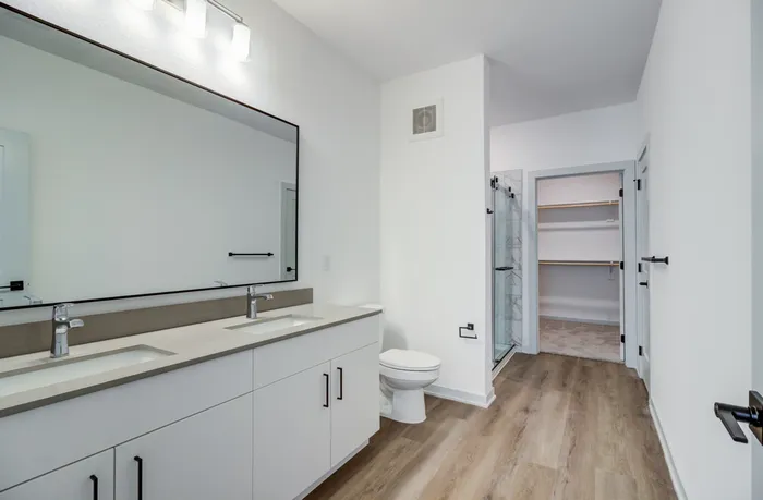 Primary bathroom with double vanity, large black-framed mirror, walk-in shower, and walk-in closet access at Garrett Forum in Fort Myers, Florida.
