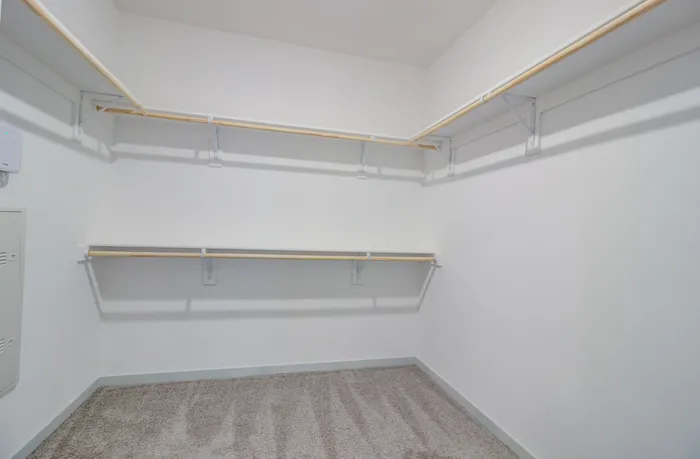 Large walk-in closet with wood rods and solid shelving on three walls, including double hanging rows on the back wall, at Garrett Forum in Fort Myers, Florida.