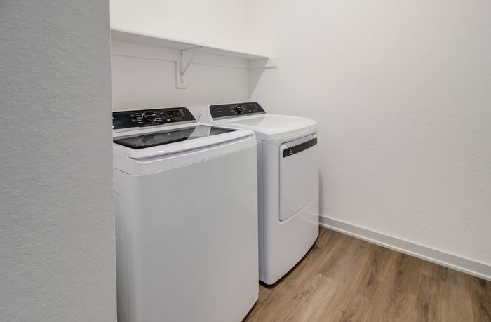 In-home laundry room with full-size washer and dryer and shelf at Garrett Forum in Fort Myers, Florida.
