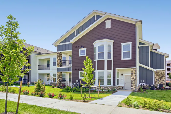 Angled exterior view of Garrett Harvest Junction West apartment building in Longmont, CO showing private unit entrances, bay window detail, and manicured lawn