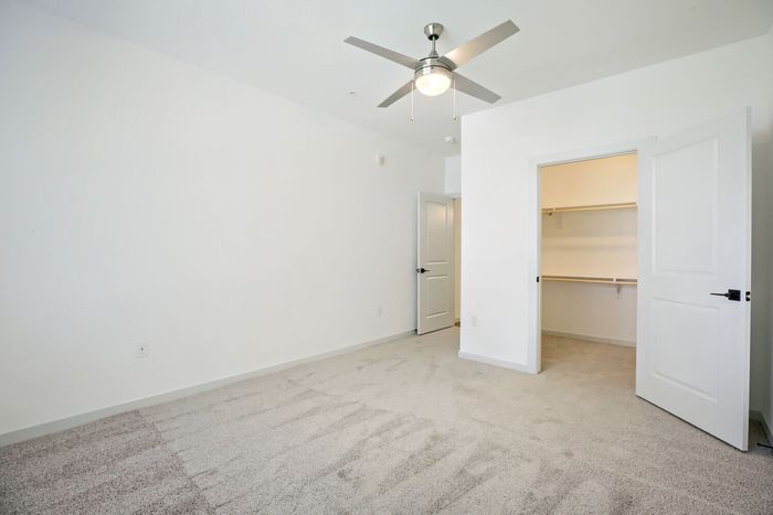 Carpeted bedroom showing walk-in closet with built-in shelving at Garrett Harvest Junction West apartments in Longmont, CO
