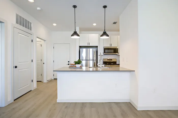 Modern kitchen with white cabinetry, quartz-style countertops, herringbone tile backsplash, stainless appliances, and black pendant lights at Garrett Harvest Junction West Longmont CO