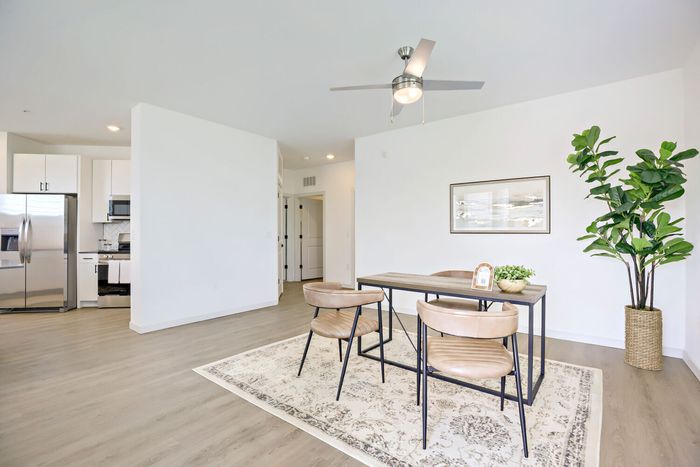 Staged dining area with wood table, leather chairs, and area rug next to open kitchen with stainless appliances at Garrett Harvest Junction West Longmont CO