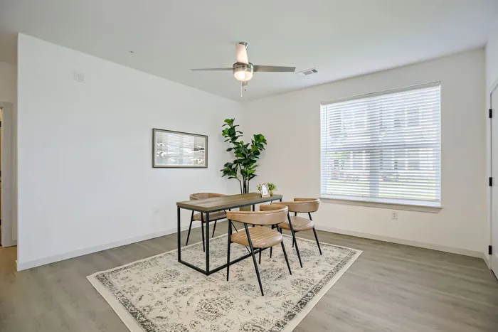 Bright staged dining room with large window, wood table, leather chairs, and fiddle leaf fig tree at Garrett Harvest Junction West apartments Longmont CO