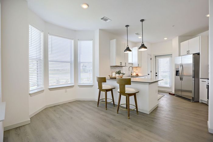 Kitchen with bay window nook, white peninsula with barstools, pendant lights, herringbone backsplash, and stainless steel refrigerator at Garrett Harvest Junction West Longmont CO