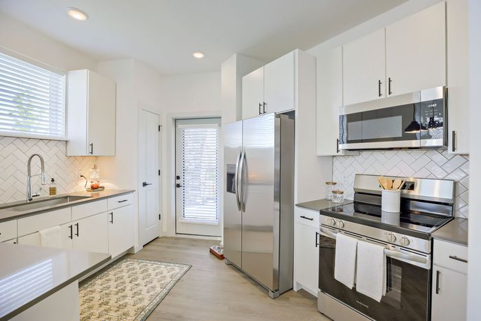 Full kitchen view with stainless steel refrigerator, range, over-range microwave, herringbone tile backsplash, white shaker cabinets, and back door at Garrett Harvest Junction West apartments Longmont CO