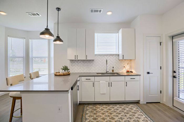 Kitchen peninsula with a dishwasher, pendant lights, herringbone backsplash, and bay window view at Garrett Harvest Junction West apartments in Longmont, CO