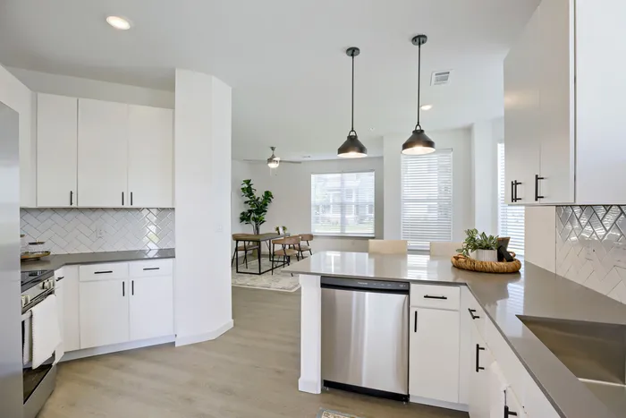 Open concept kitchen with stainless dishwasher, pendant lights, white cabinetry, and view through to dining room at Garrett Harvest Junction West apartments Longmont CO
