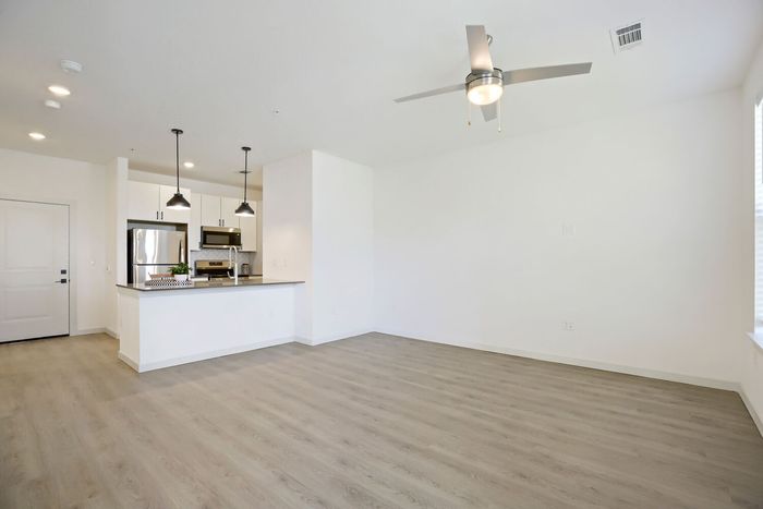 Wide open living room with luxury vinyl plank flooring looking toward kitchen peninsula and pendant lights at Garrett Harvest Junction West in Longmont, CO