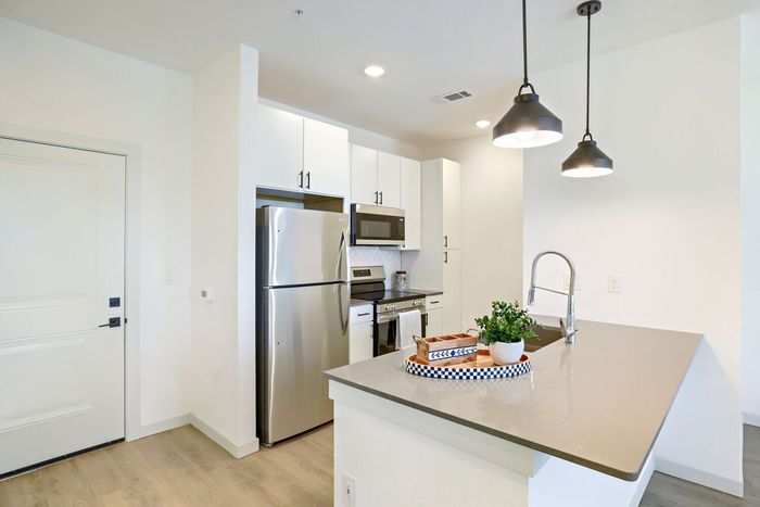 Close-up of kitchen peninsula countertop with stainless sink, pendant lights, stainless refrigerator and range in background at Garrett Harvest Junction West Longmont CO