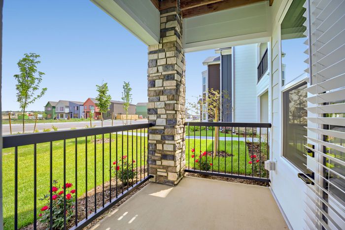 Private covered porch or balcony with stone column, black iron railing, and view of landscaped lawn and Harvest Junction neighborhood at Garrett Harvest Junction West Longmont CO