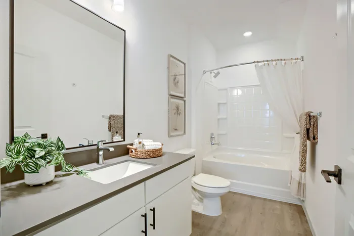 Staged full bathroom with soaking tub, shower, large framed mirror, white vanity cabinet with gray countertop at Garrett Harvest Junction West apartments Longmont CO