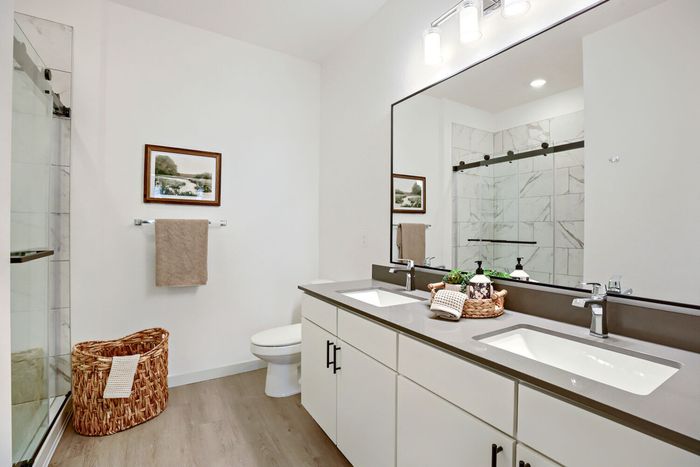 Primary bathroom with double sink vanity, large frameless mirror, walk-in glass shower with tile surround at Garrett Harvest Junction West apartments Longmont CO
