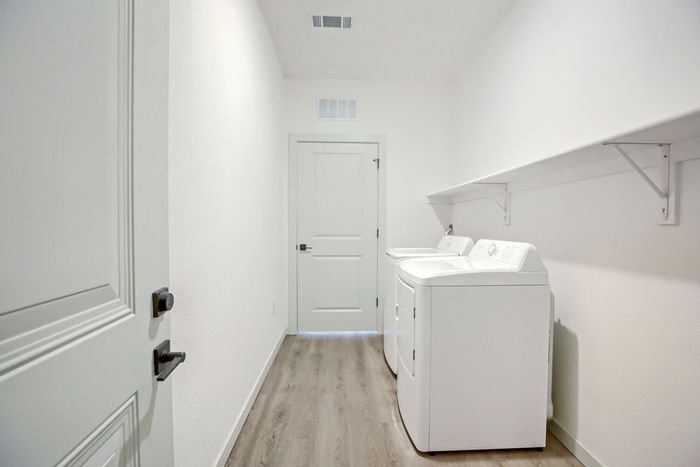 In-unit laundry room with full-size washer and dryer and overhead storage shelf at Garrett Harvest Junction West apartments Longmont CO
