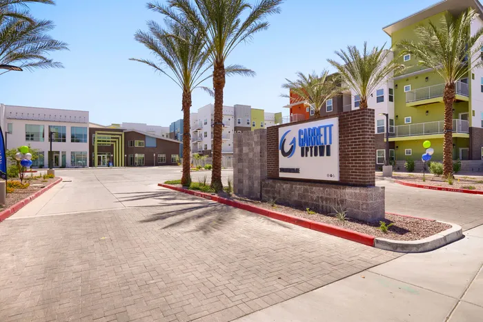 Garrett Uptown apartment community entrance with palm trees and brick monument sign in Chandler, Arizona