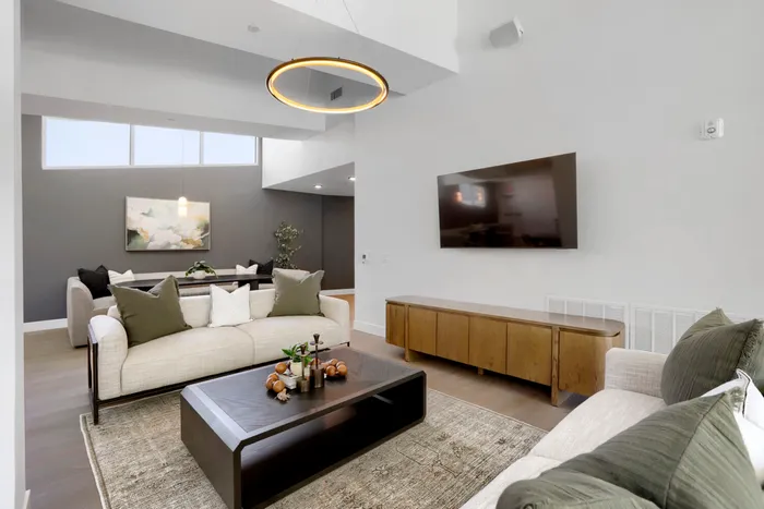 Garrett Uptown clubhouse living room with linen sofa, dark wood coffee table, ring pendant light, and wall-mounted TV in Chandler, AZ