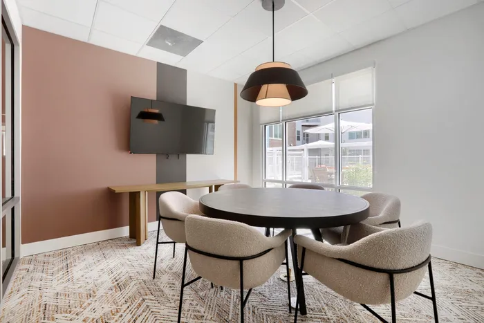Garrett Uptown clubhouse private conference room with round table, boucle chairs, wall-mounted TV, and mauve accent wall in Chandler, AZ