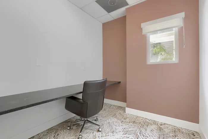 Garrett Uptown resident business center private work pod with built-in desk, leather task chair, and mauve accent wall in Chandler, AZ
