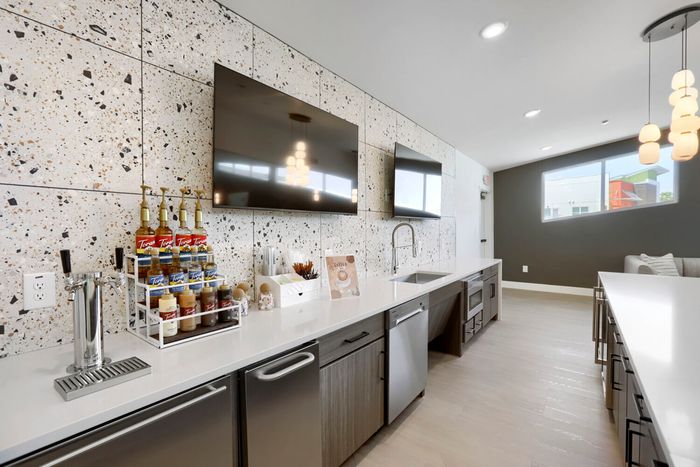 Garrett Uptown clubhouse coffee bar with Torani syrup station, draft tap, terrazzo tile wall, and dual wall-mounted TVs in Chandler, AZ
