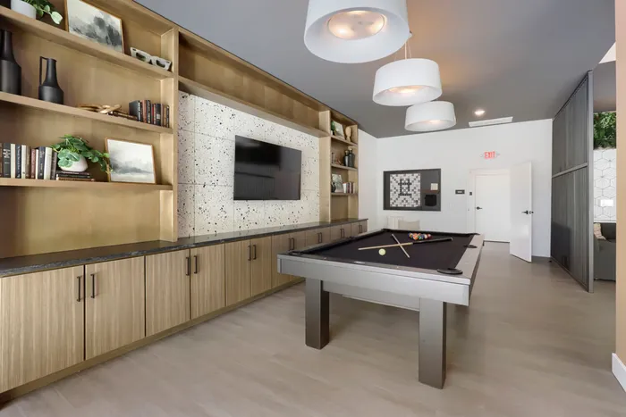 Garrett Uptown clubhouse billiards and game room with pool table, terrazzo TV wall, brass built-in shelving, and board games in Chandler, AZ