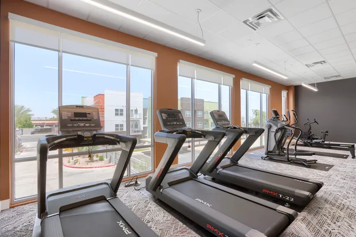 Garrett Uptown fitness center cardio row with PMX treadmills, ellipticals, and rowing machine facing floor-to-ceiling windows in Chandler, AZ