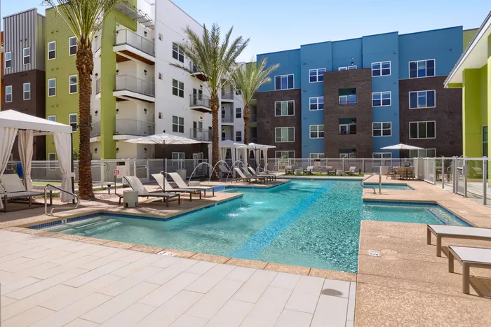 Garrett Uptown resort-style swimming pool with palm trees, lounge chairs, pool cabanas, and water features surrounded by apartment buildings in Chandler, AZ