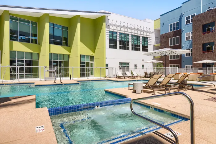 Garrett Uptown resort pool and spa hot tub with lounge chairs, market umbrellas, and clubhouse building in Chandler, AZ