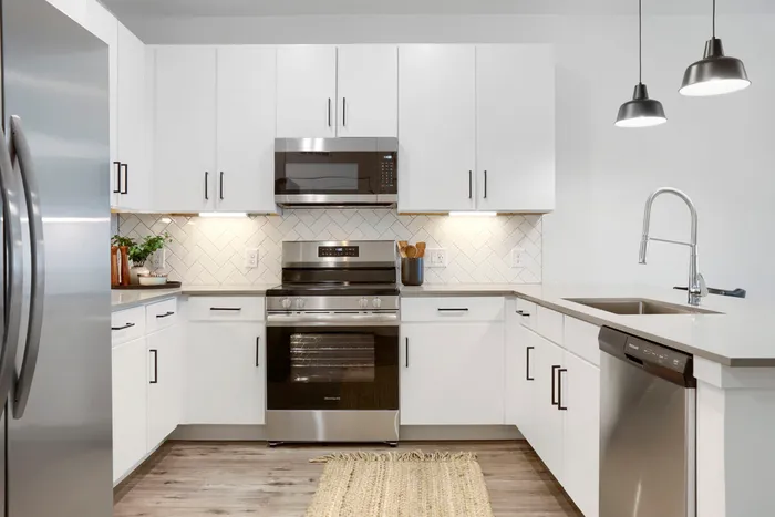 Garrett Uptown B2 apartment kitchen with white shaker cabinets, stainless steel appliances, herringbone tile backsplash, quartz countertops, and black pendant lights in Chandler, AZ