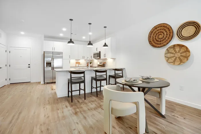 Garrett Uptown B2 apartment open kitchen with white island bar seating, stainless appliances, pendant lighting, and adjacent dining area with wood-look floors in Chandler, AZ