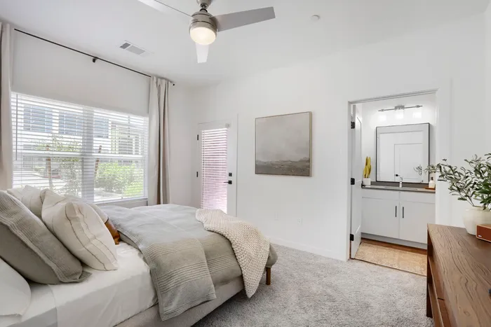 Garrett Uptown B2 primary bedroom with plush carpet, ceiling fan, large windows, and en suite bathroom access in Chandler, AZ