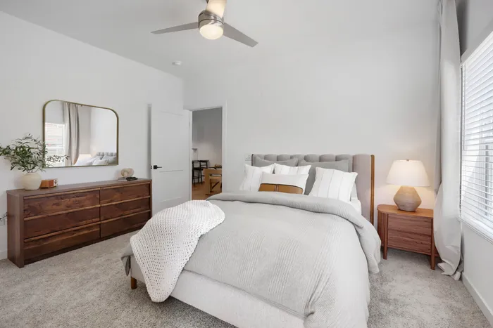 Garrett Uptown B2 primary bedroom with vaulted ceiling, upholstered bed, walnut dresser, ceiling fan, and large windows in Chandler, AZ