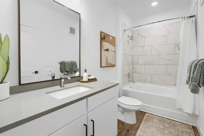 Garrett Uptown B2 primary bathroom with quartz countertop, black-framed mirror, white vanity, and marble-look tile tub surround in Chandler, AZ