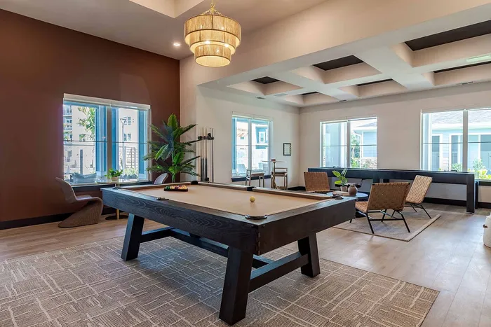 Game room with billiards table, statement chandelier, and lounge seating at Garrett Gateway in Fort Myers, FL
