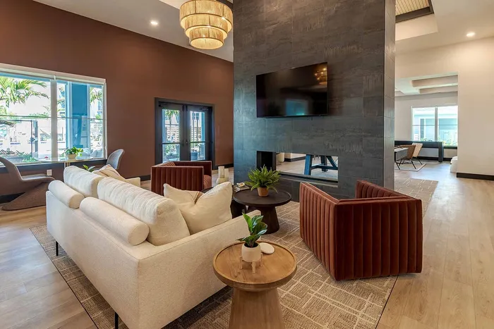 Open clubhouse lounge with double-sided fireplace, TV, and modern seating at Garrett Gateway apartments in Fort Myers, FL