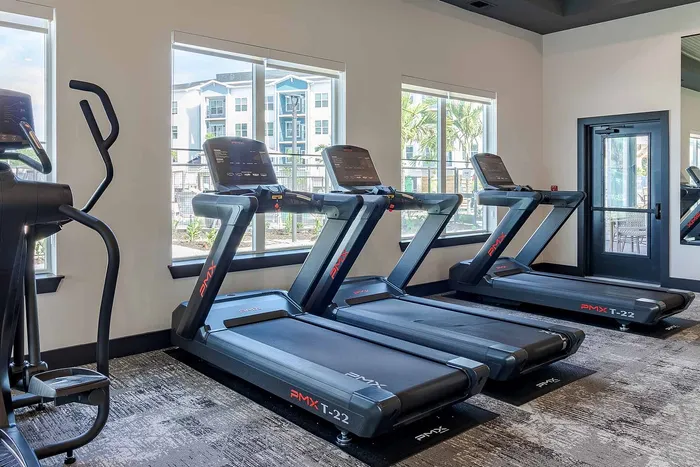 Row of PMX treadmills facing bright windows in the fitness center at Garrett Gateway apartments in Fort Myers, FL