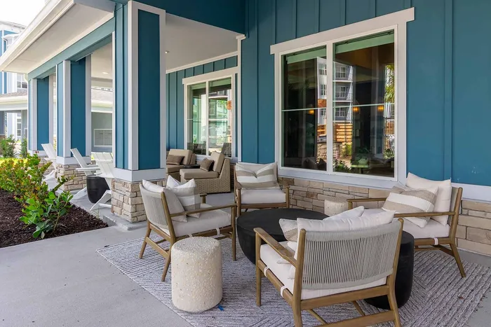 Covered porch with cushioned lounge chairs and Adirondack seating at Garrett Gateway apartments in Fort Myers, FL