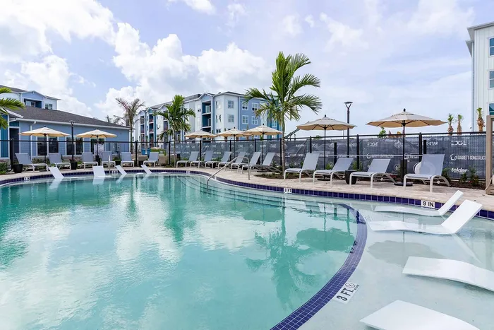Resort-style pool with tanning ledge, lounge chairs, and umbrellas at Garrett Gateway apartments in Fort Myers, FL