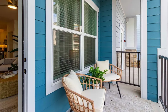 Private balcony with woven chairs and coastal blue siding at Garrett Gateway apartments in Fort Myers, FL