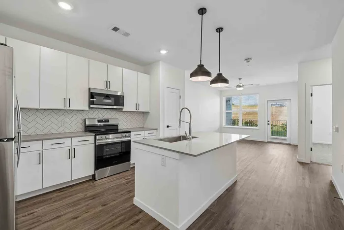 Open-concept A1 kitchen and living area at Garrett Fillmore with a center island, stainless appliances, and patio door.
