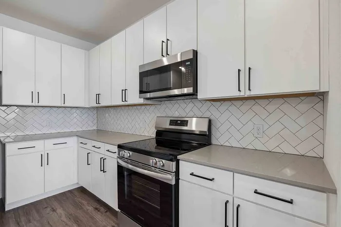 A1 kitchen at Garrett Fillmore with a stainless steel electric range, white cabinets, and herringbone tile backsplash.
