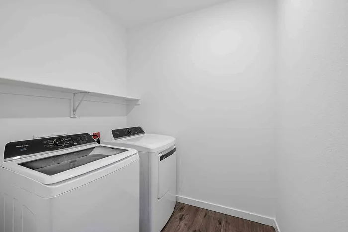 Dedicated laundry room in the C1 three-bedroom at Garrett Fillmore with a full-size washer and dryer and shelf above.