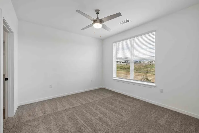 Carpeted primary bedroom in the C1 three-bedroom at Garrett Fillmore with a ceiling fan and a large window.