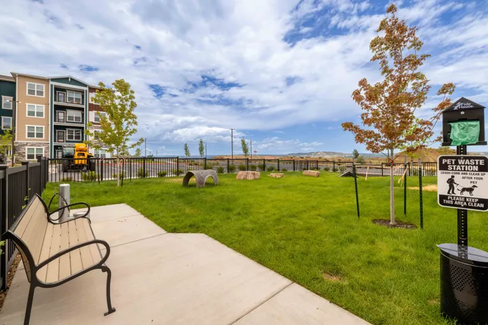 Fenced dog park at Garrett Fillmore in Colorado Springs with agility equipment, a bench, and a pet waste station.