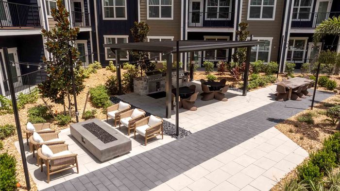Outdoor kitchen with two built-in stainless steel grills under a covered pavilion, dining tables, and a lounge area around a fire pit