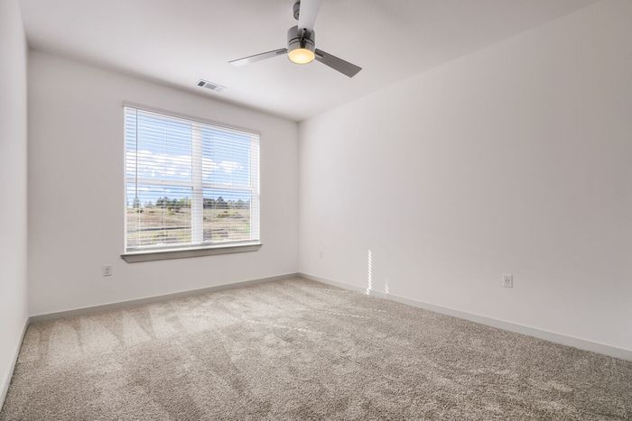 Third-floor bedroom at Garrett North Powers with carpet, ceiling fan, and a window view of open hillside and trees