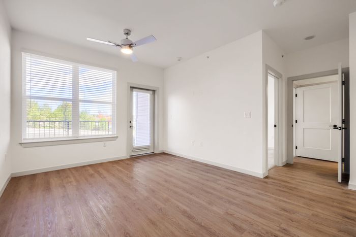 A1 one-bedroom living room at Garrett North Powers with wood-style flooring, ceiling fan, large window, and patio door