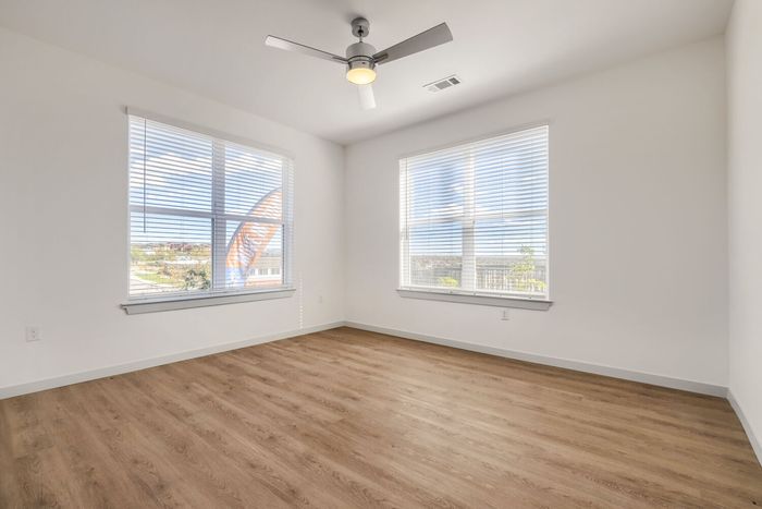 C1 three-bedroom living room at Garrett North Powers with windows on two walls, ceiling fan, and wood-style flooring