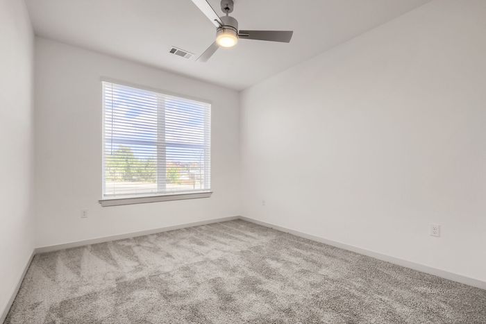 Bedroom in a B1 two-bedroom at Garrett North Powers with plush carpet, ceiling fan, and large window