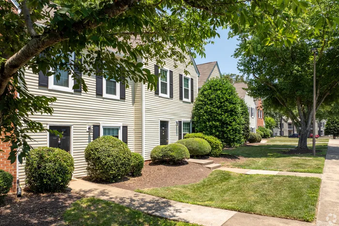 Elegant townhouse with manicured gardens and shaded pathway on a sunny day.